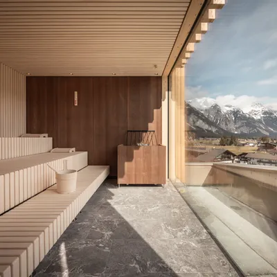 Modern wooden sauna with panoramic window overlooking alpine village and snow-capped mountains
