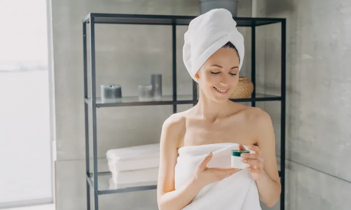 Frau im Handtuch hält Hautpflegecreme im modernen Badezimmer