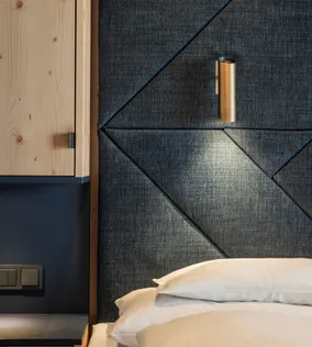 Modernes Hotelzimmer mit gepolstertem dunklem Stoffkopfteil und integrierter Leselampe