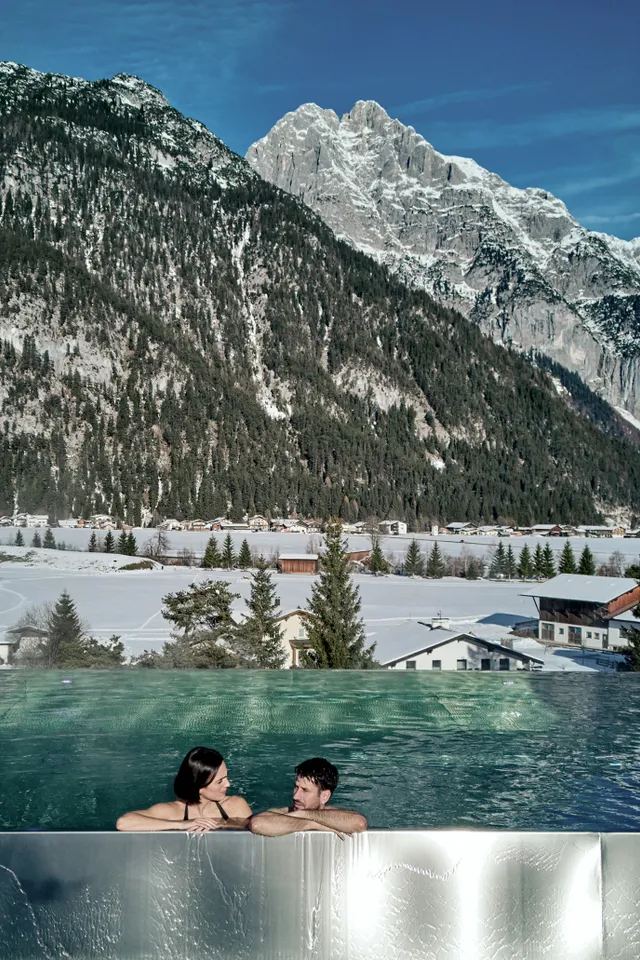 Couple relaxing in rooftop infinity pool overlooking snowy alpine mountain landscape