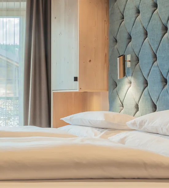 Modern hotel bed with white pillows and padded blue headboard with built-in reading lights