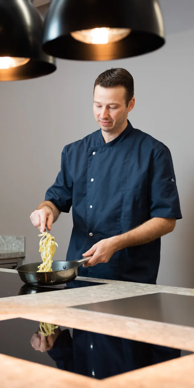 Chef in modern kitchen cooking pasta with vegetables and oils on counter