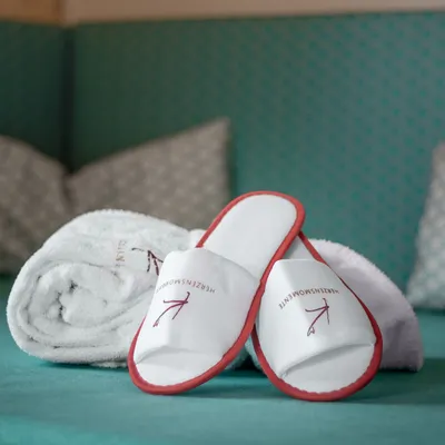 Weiße Hotelslipper mit rotem Rand und Handtuch auf türkisfarbenem Loungesessel