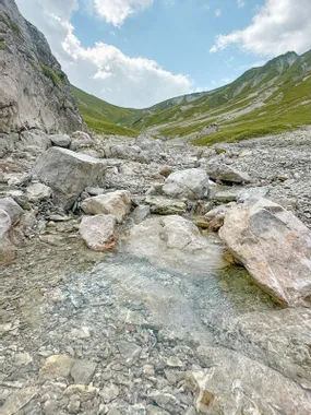 Clear mountain stream flowing through rocky alpine valley under blue sky