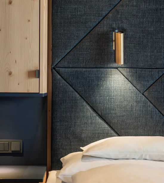 Modernes Hotelzimmer mit gepolstertem dunklem Stoffkopfteil und integrierter Leselampe