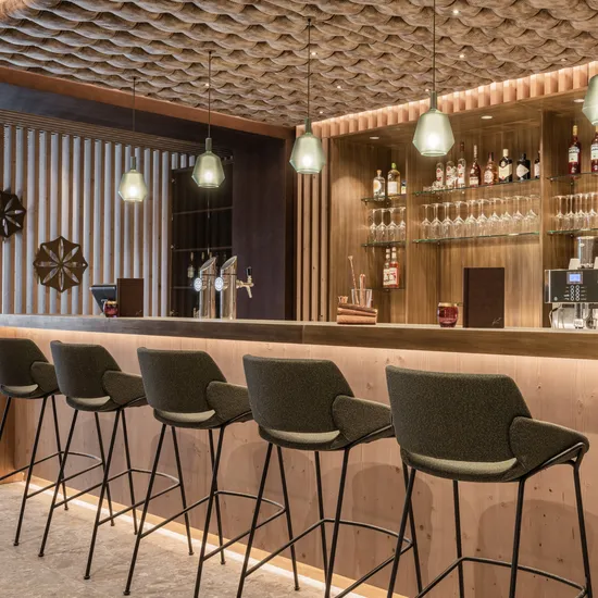 Moderne Hotelbar aus Holz mit Barhockern, Hängelampen und bestückten Regalen mit Spirituosen und Gläsern