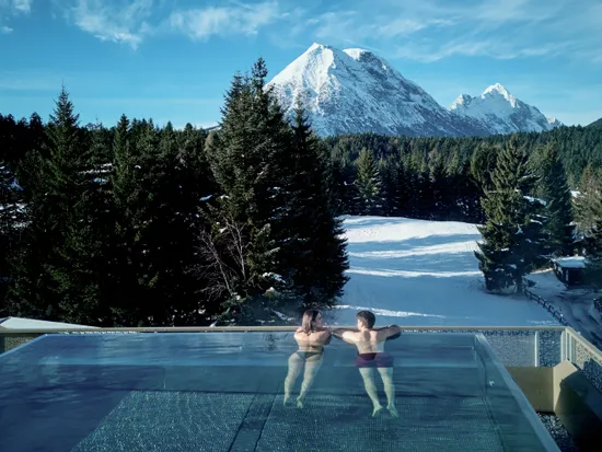 Paar entspannt im beheizten Infinity-Pool mit Blick auf verschneite Alpen und Wald