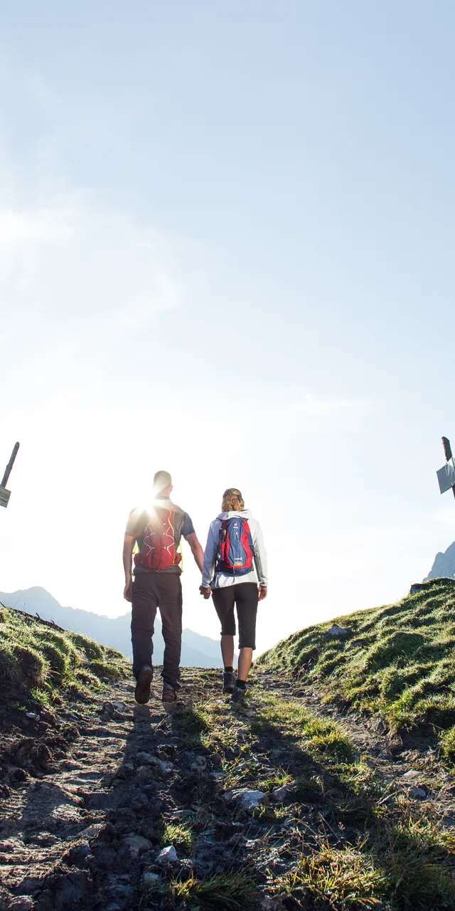 Couple hiking on a mountain trail with backpacks under clear blue sky