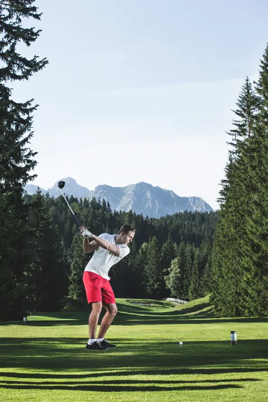 Golfer in red shorts swinging a golf club on a scenic mountain course
