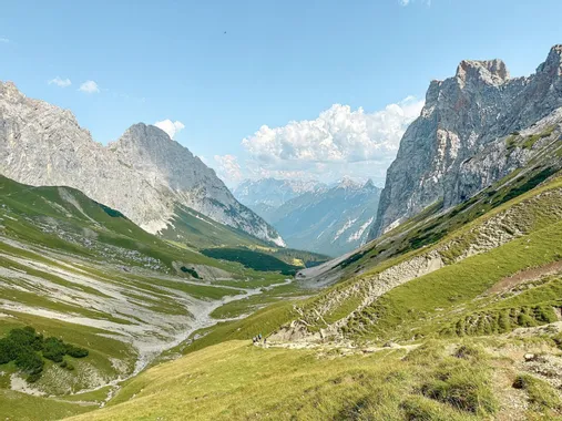 Panoramablick auf ein Alpental mit grünen Hängen und schroffen Berggipfeln unter blauem Himmel