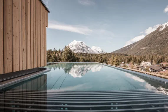 Infinity pool with mountain view near wooden building in alpine resort