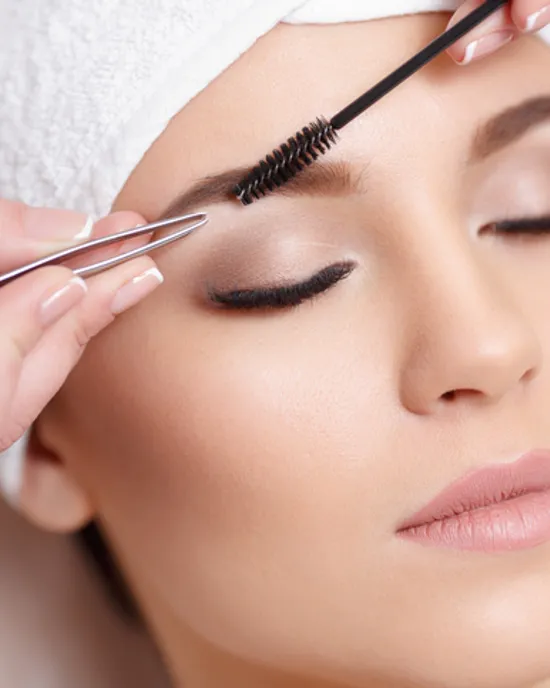 Woman receiving eyebrow shaping with tweezers and brush at beauty salon