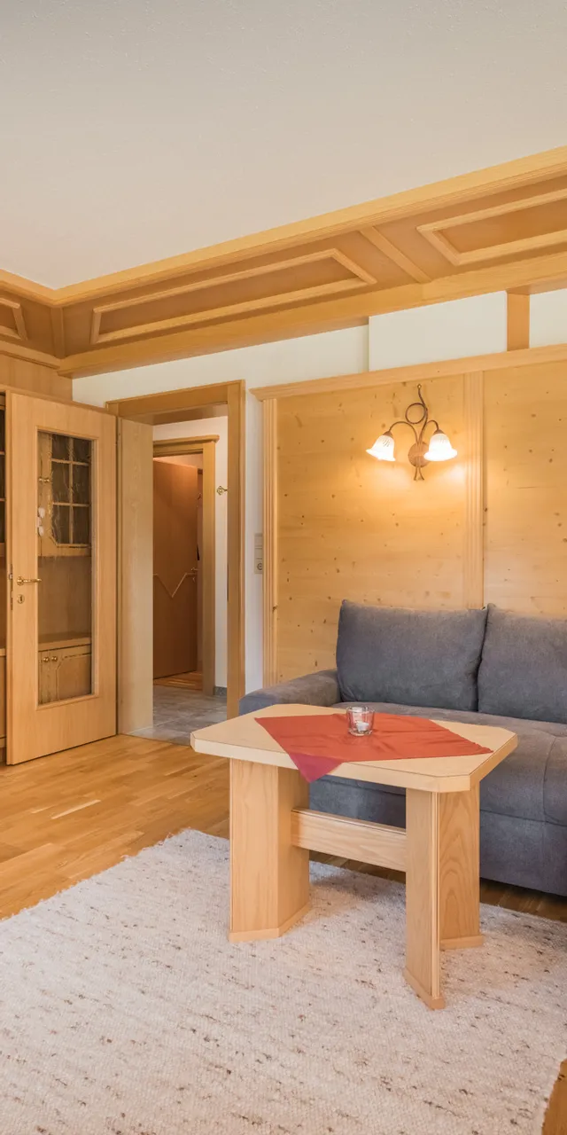 Gemütliches Wohnzimmer mit Holzmöbeln, Ecksofa, Flachbildfernseher und warmem Licht