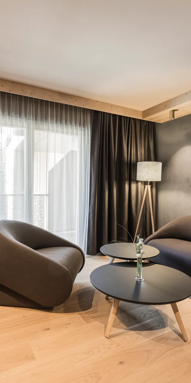 Modern hotel living room with dark furniture, wood flooring, and floor-to-ceiling curtains