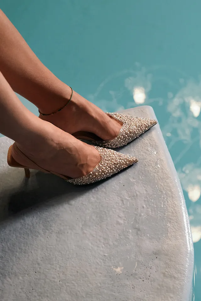 Frau mit glitzernden High Heels und Kronleuchter-Spiegelung im türkisfarbenen Wasser