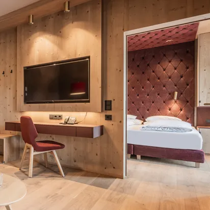 Moderne Hotelsuite mit Holzeinrichtung, roten Möbeln, Flachbildfernseher und verbundenem Schlafzimmer