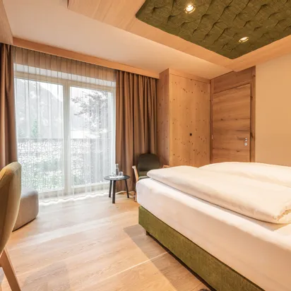 Modernes Hotelzimmer mit Holzausstattung, Doppelbett, Schreibtisch, Fernseher und Bergblick durchs Fenster