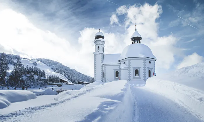 Snow-covered alpine church with domed tower in a winter mountain landscape