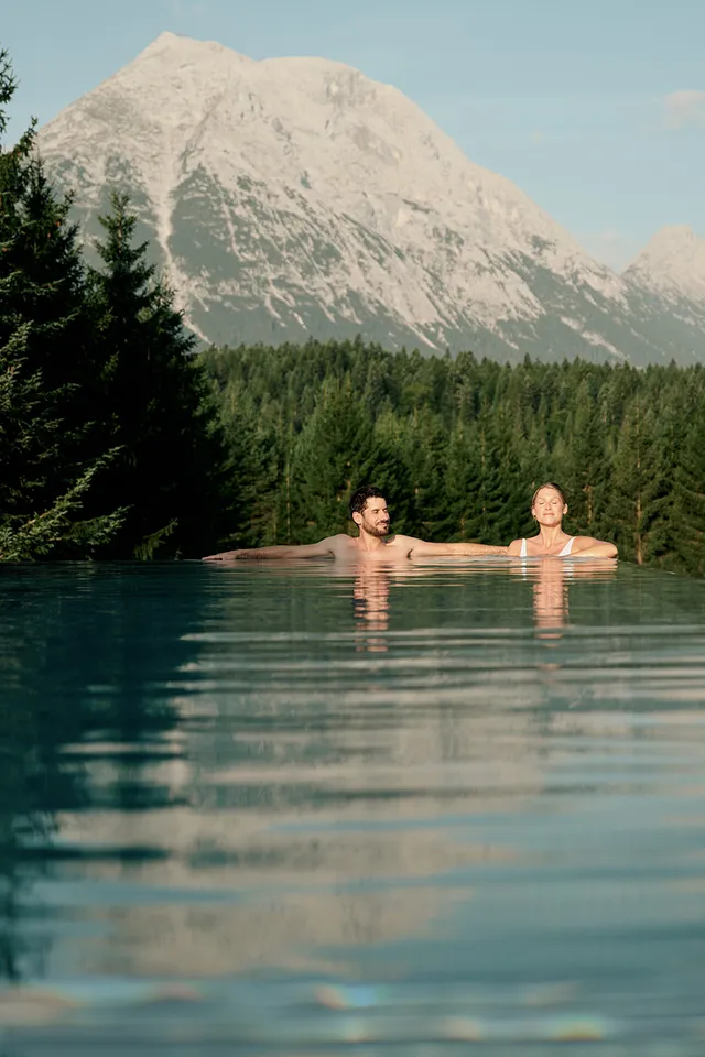 Couple relaxing in infinity pool with mountain and forest view in summer
