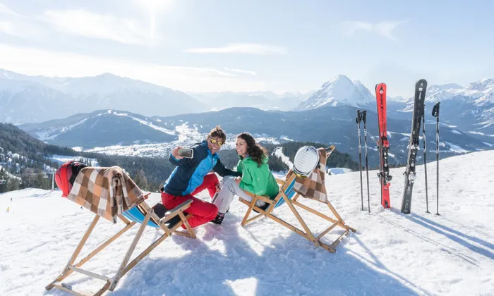 Couple taking selfie on deck chairs in sunny ski resort with mountain view