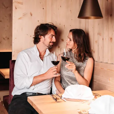 Romantisches Paar stößt mit Rotwein in gemütlicher Holzrestaurantkabine an