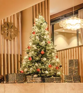 Geschmückter Weihnachtsbaum mit Lichtern und roten Kugeln von Geschenken umgeben im Innenbereich