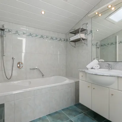 Modern attic bathroom with bathtub, sink, large mirror, and folded towels