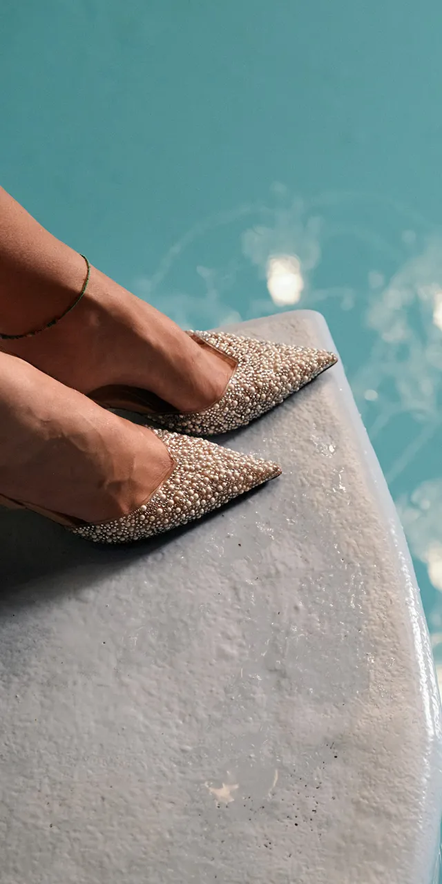 Frau mit glitzernden High Heels und Kronleuchter-Spiegelung im türkisfarbenen Wasser