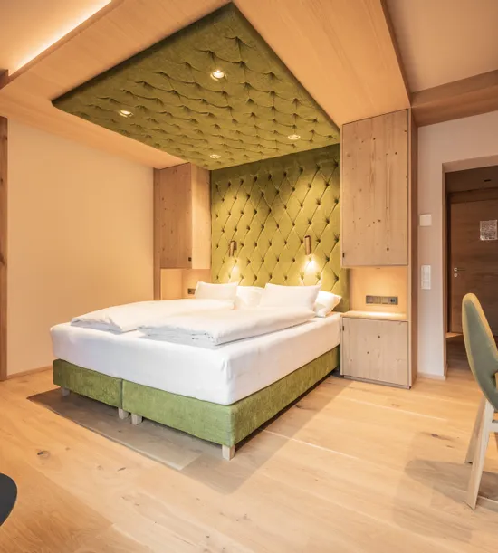 Modernes Hotelzimmer mit grünem Polsterbett, Holzmöbeln und gemütlicher Beleuchtung