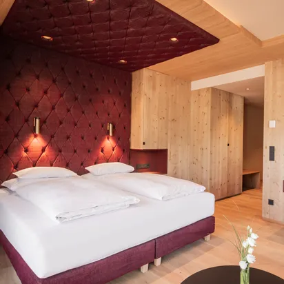 Modern hotel room with twin bed, wood paneling, mounted TV and burgundy accents