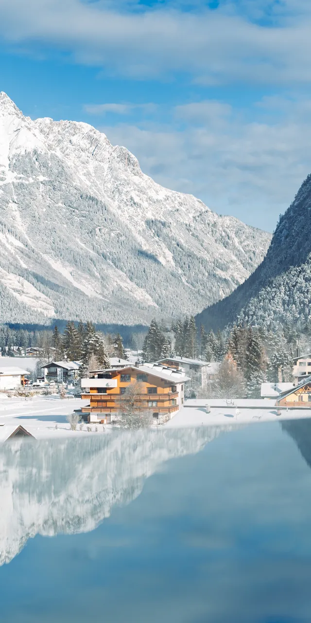 Schneebedecktes Alpendorf mit Holzhütten und Bergspiegelung im gefrorenen See