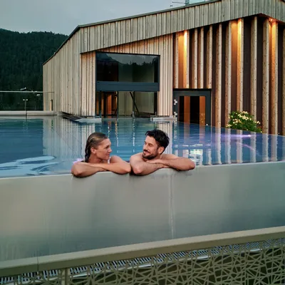 Paar entspannt im Infinity-Pool auf dem Dach eines luxuriösen Alpinresorts mit Holzarchitektur