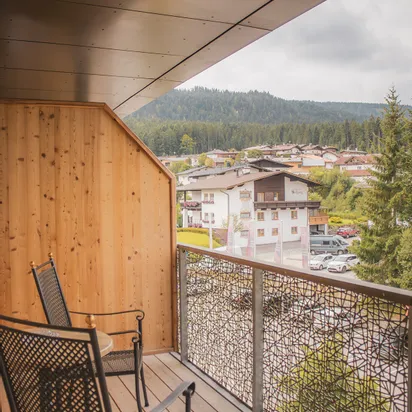 Wooden balcony with two chairs overlooking Alpine village and forested hills