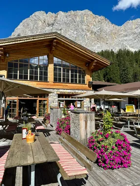 Wooden alpine restaurant with outdoor seating and pink flowers near mountain backdrop