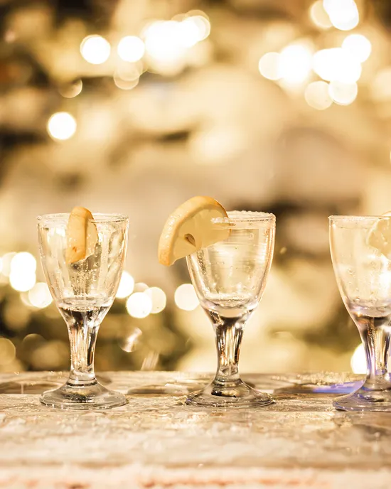 Four glasses with lemon slices on snowy bar against festive lights