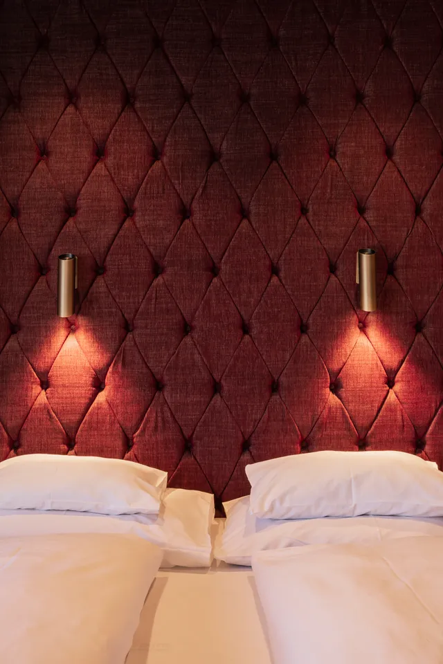 Hotel room with twin beds, quilted burgundy headboard and warm wall lighting