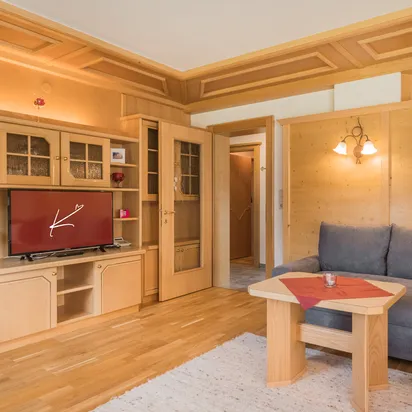 Gemütliches Wohnzimmer mit Holzmöbeln, Ecksofa, Flachbildfernseher und warmem Licht