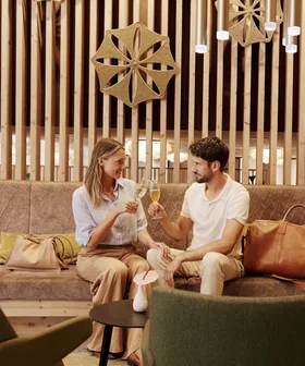 Paar stößt mit Champagner in moderner Hotellounge mit Holzdekor an