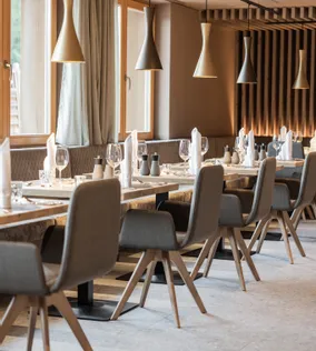 Modern restaurant interior with wooden tables, grey chairs, and elegant pendant lighting