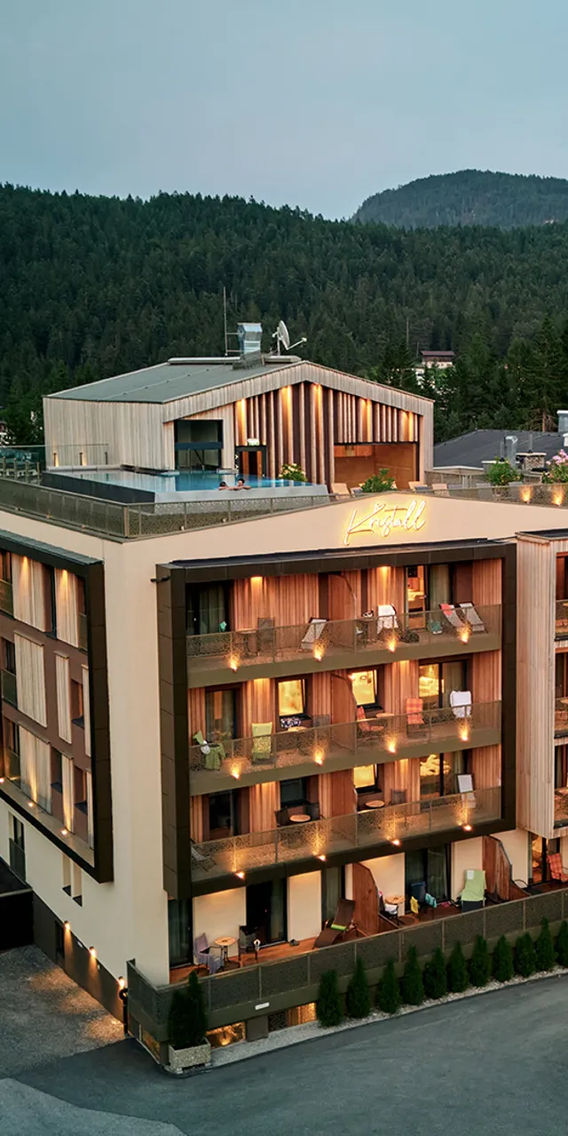 Modern alpine hotel with balconies and rooftop terrace surrounded by mountains and forest