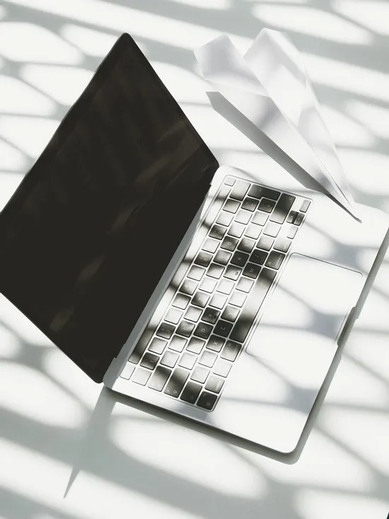 Laptop with paper airplane on keyboard under striped sunlight shadows