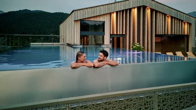 Paar entspannt im Infinity-Pool auf dem Dach eines luxuriösen Alpinresorts mit Holzarchitektur