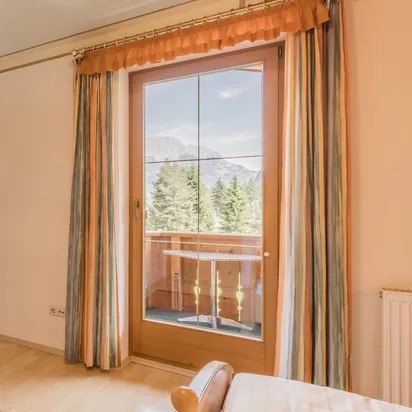 Helles Alpenhotelzimmer mit Holzmöbeln und Bergblick durch Balkontür