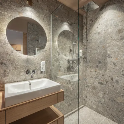 Modern bathroom with terrazzo tiles, round mirror, glass shower and wooden vanity