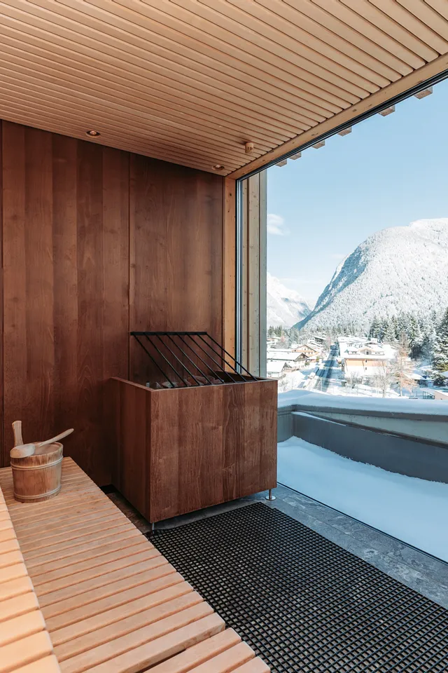 Moderne Holzsauna mit Panoramafenster und Blick auf verschneites Alpendorf und Berge