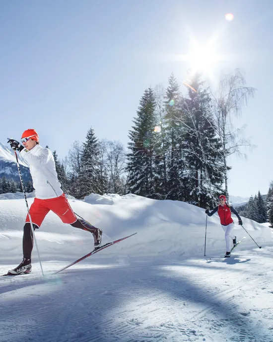 Zwei Personen beim Langlaufen an einem sonnigen Wintertag in verschneiter Berglandschaft