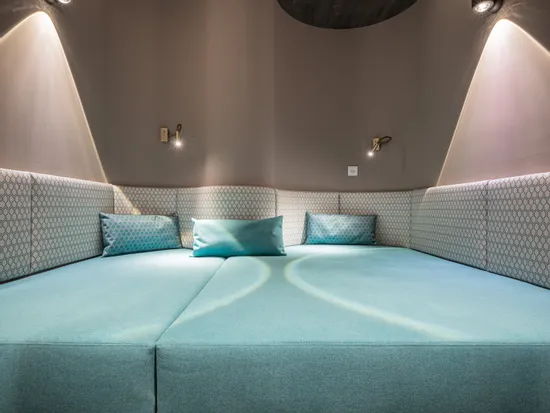 Modernes Wellness-Liegebett mit türkisen Kissen und stimmungsvoller Beleuchtung im Spa-Raum