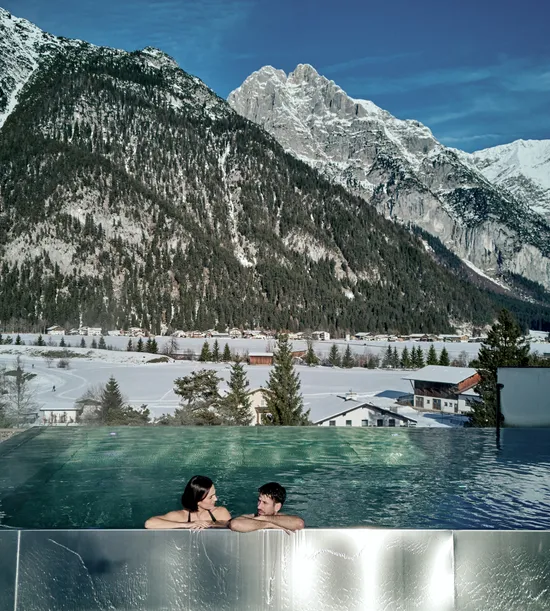 Couple relaxing in rooftop infinity pool overlooking snowy alpine mountain landscape
