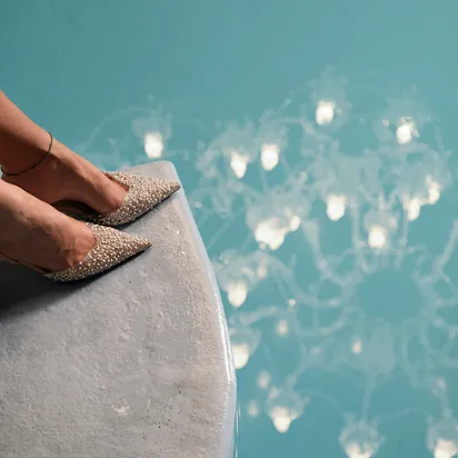 Frau mit glitzernden High Heels und Kronleuchter-Spiegelung im türkisfarbenen Wasser