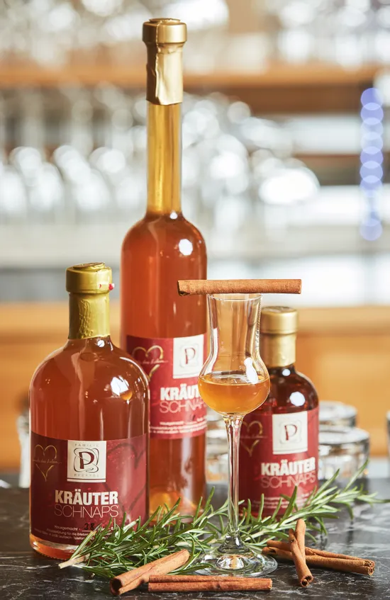 Bottles of herbal schnapps with a filled glass, cinnamon sticks and rosemary on a dark surface